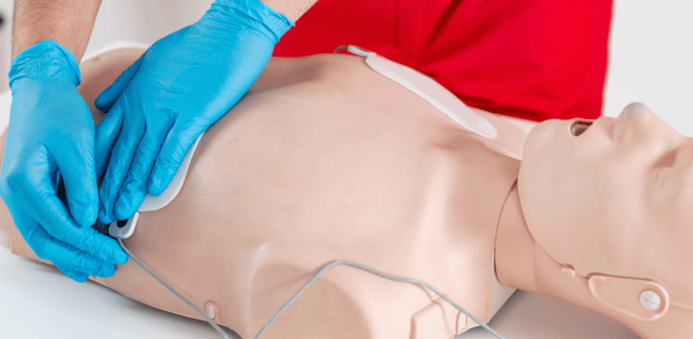 Manos con guantes azules usando un desfibrilador portátil